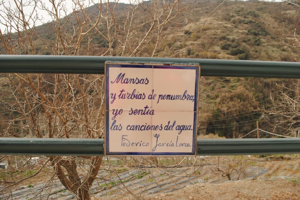 Quinto verso del Paseo Federico García Lorca en Pampaneira que dice: Mansas y turbias de penumbra, yo sentía las canciones del agua.